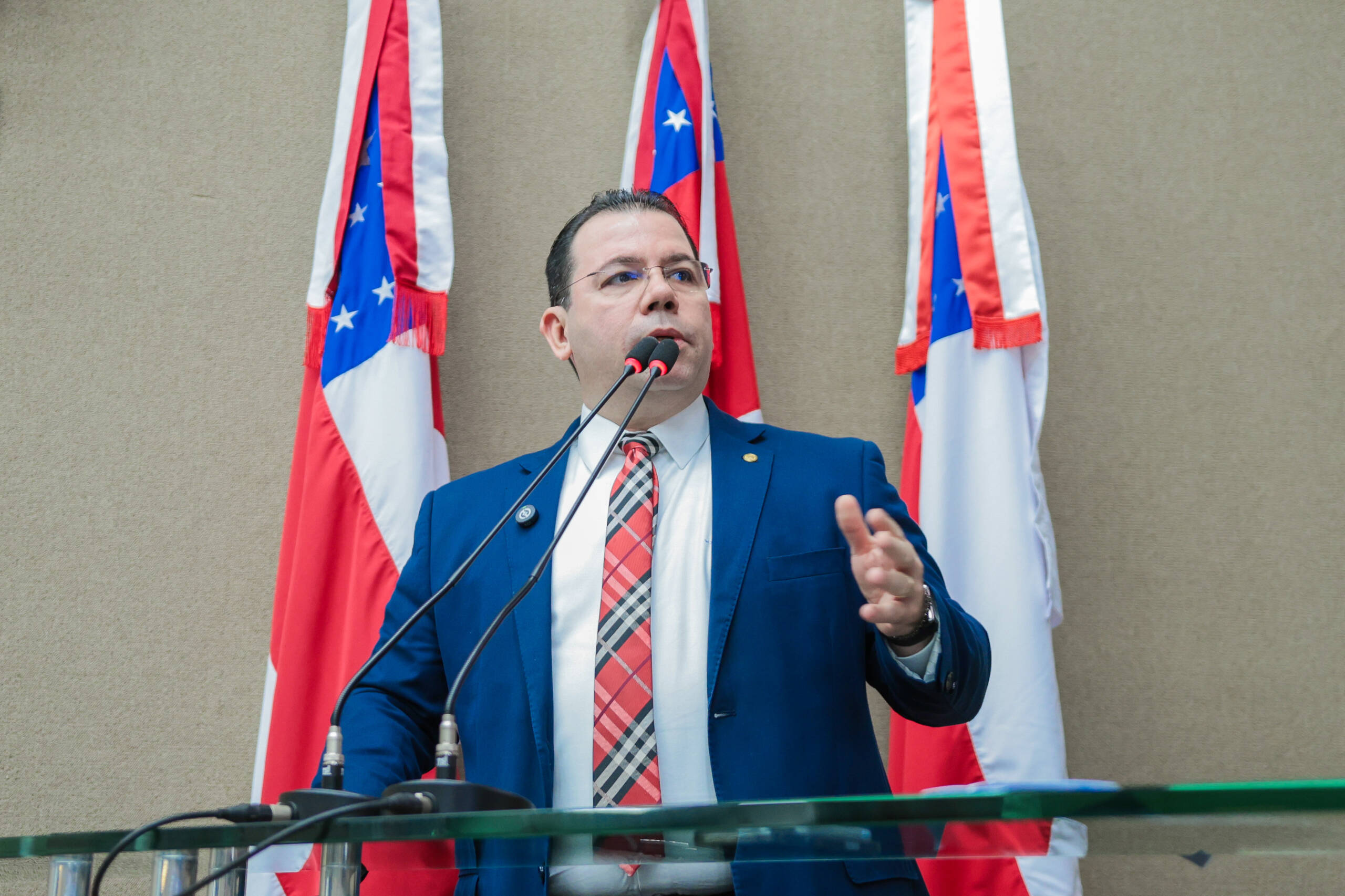 Wilker Barreto ocupa a tribuna da Assembleia Legislativa usando paletó azul-marinho e gravata xadrez vermelha.